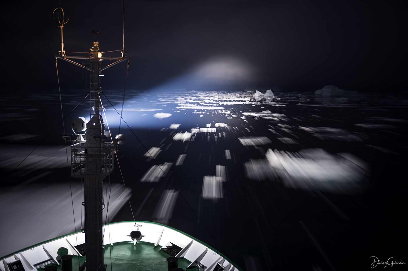 A beam of light shining from the mast on a ship out over sea ice.