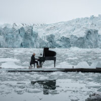 A man playing a grand piano on an island in the Arctic, surrounded by iceberg and ice floes