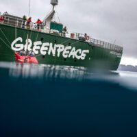 A small red submarine is lowered into the ocean from a Greenpeace ship