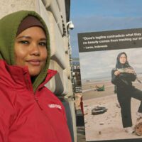 Laras Nauna, an Indonesian woman, stands in front of a large sign with a quote and photo of her criticising Dove's plastic pollution.