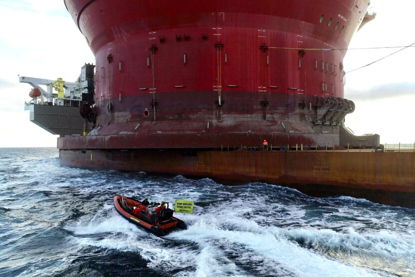 A small Greenpeace boat approaching a giant oil platform.