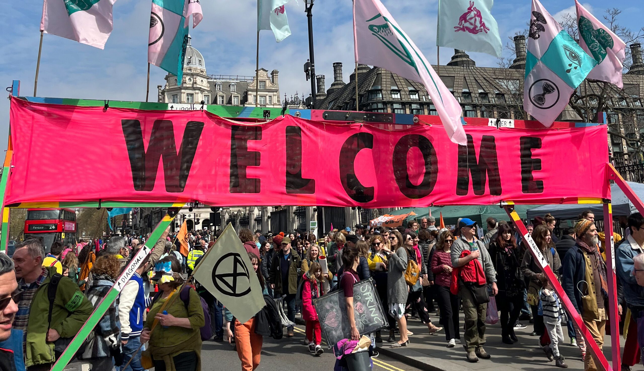 Protestors hold a giant banner saying welcome. They also have colourful flags