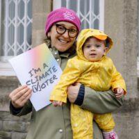 A woman holds a baby and a "I'm a climate voter" poster