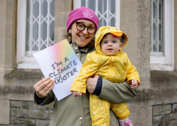 A woman holds a baby and a "I'm a climate voter" poster