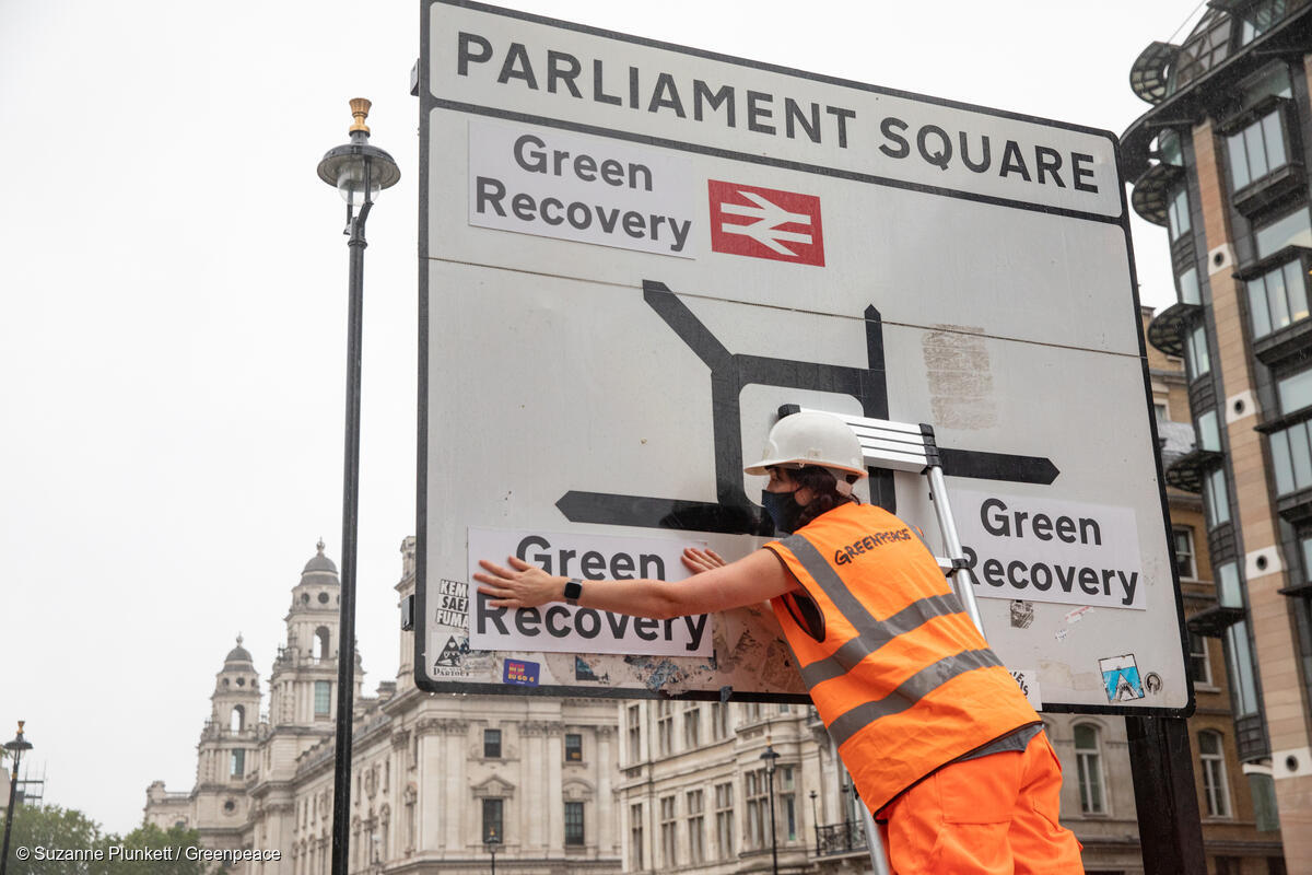 An activist replaces the destination names on a road sign in Parliament Square with labels saying 'Green Recovery'