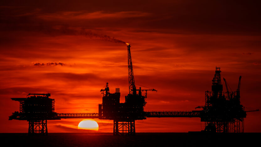 Three connected gas platforms (they look like oil rigs) against a deep red sunset.