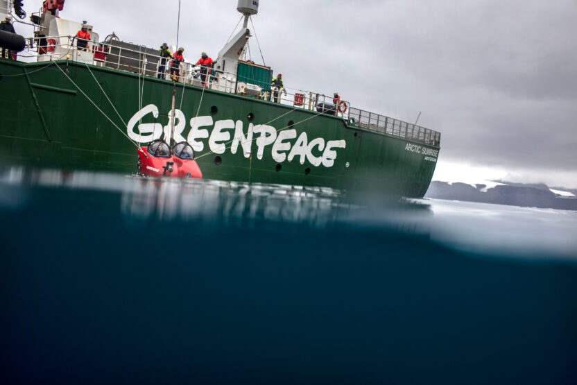 A small red submarine is lowered into the ocean from a Greenpeace ship