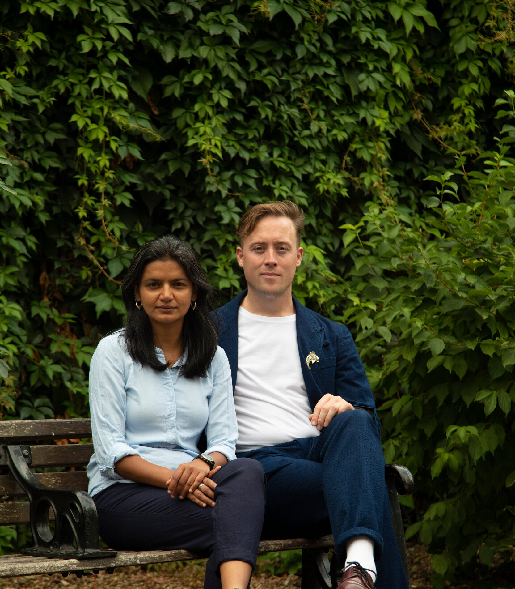 Areeba and Will sitting together on a bench outside, with dense foliage in the background