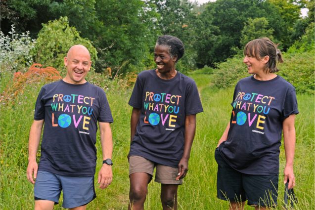 Three people walking through long grass in t-shirts that say 'protect what you love'