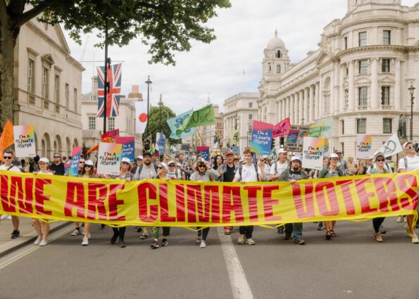 At the front of a march, a giant banner says 'we are climate voters'