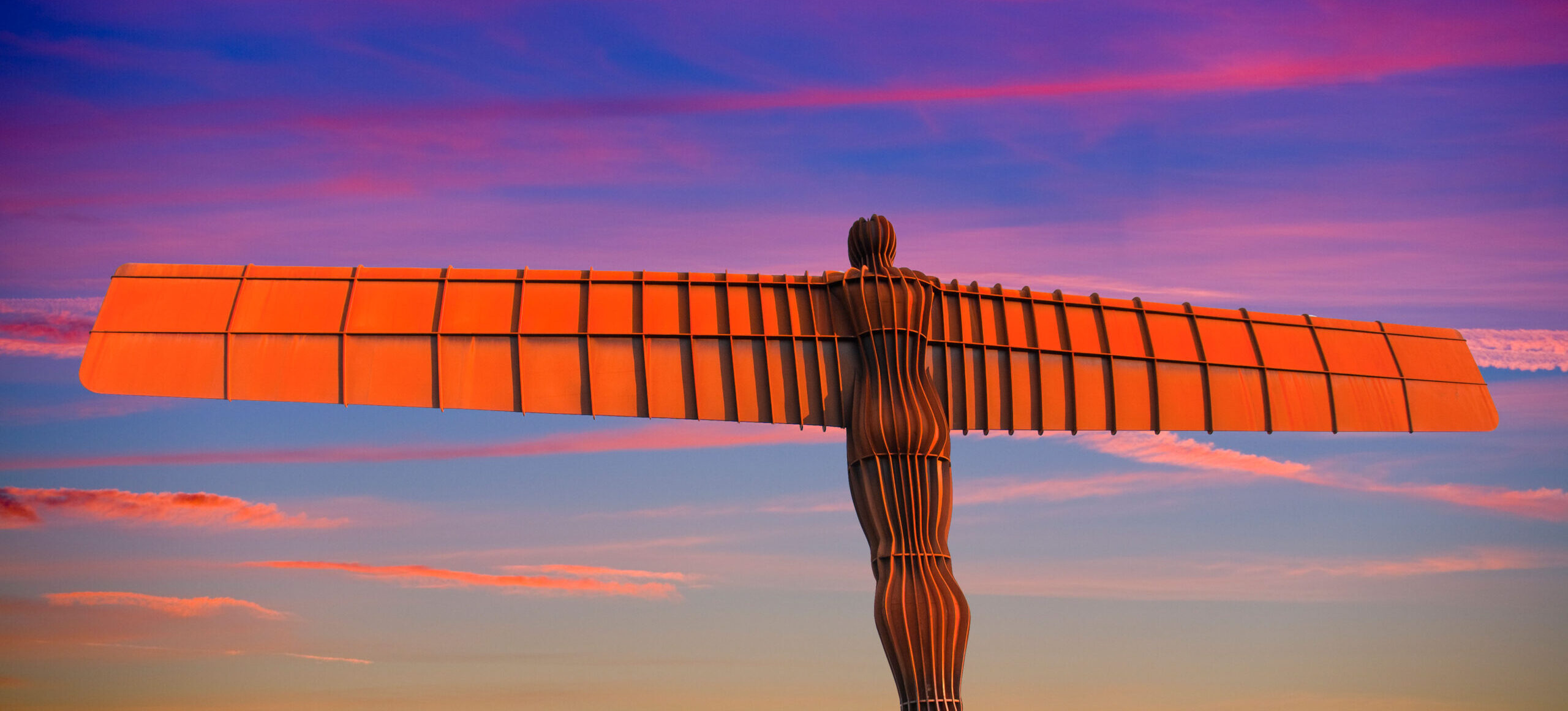 The Angel of the North, a giant metal sculpture, spreads its wings against a beautiful sunset.