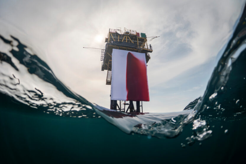 Fake blood stains a giant white fabric backdrop attached to an offshore platform in a calm ocean.
