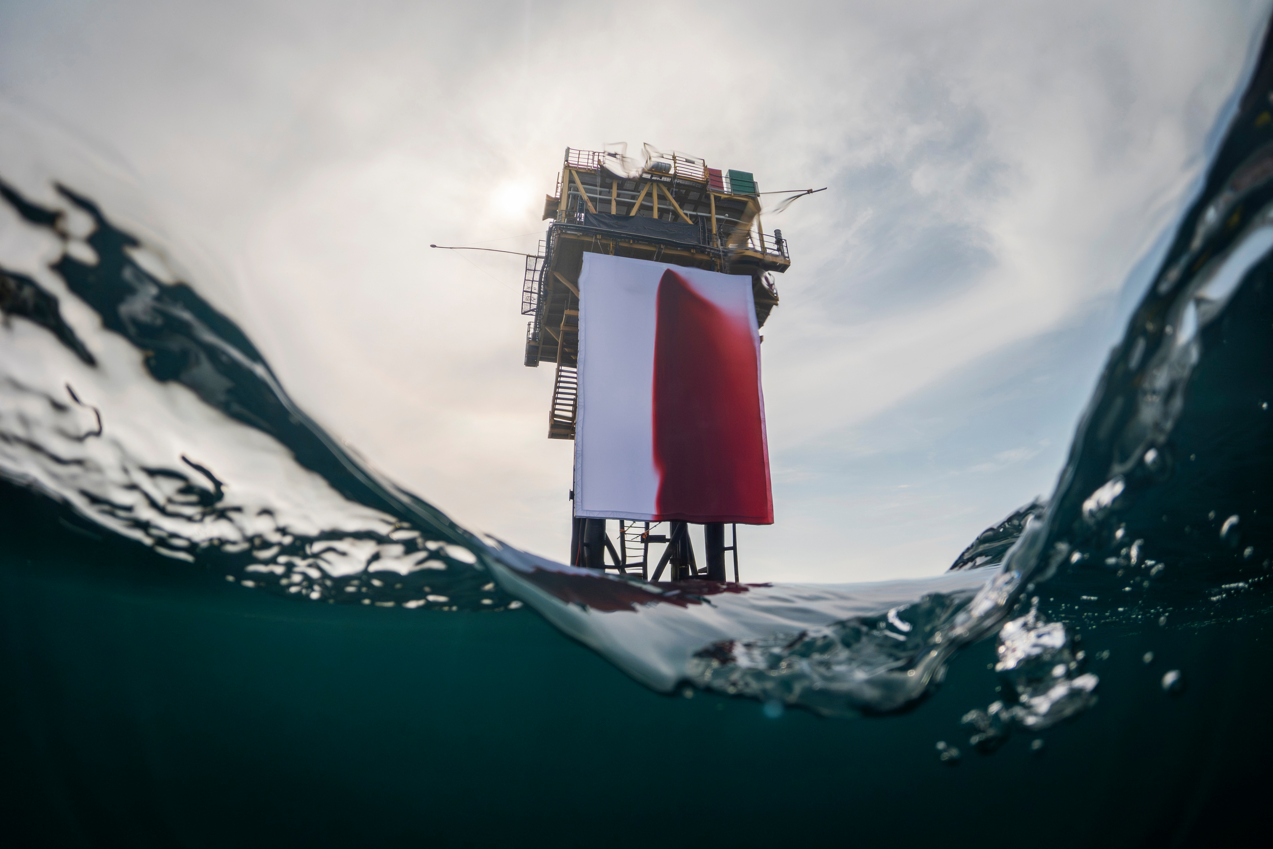 Fake blood stains a giant white fabric backdrop attached to an offshore platform in a calm ocean.